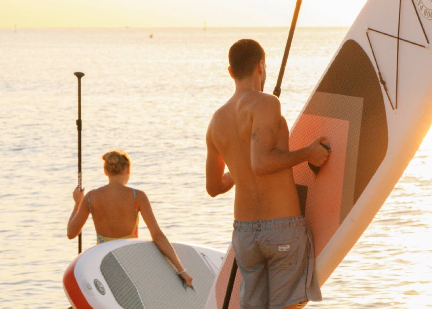 Two people carrying SUP paddleboards down to the water