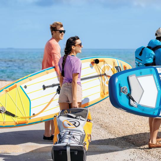 3 people with SUP gear, one holding a paddleboard backpack