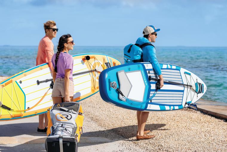 Three people holding SUP equipment looking out at the ocean