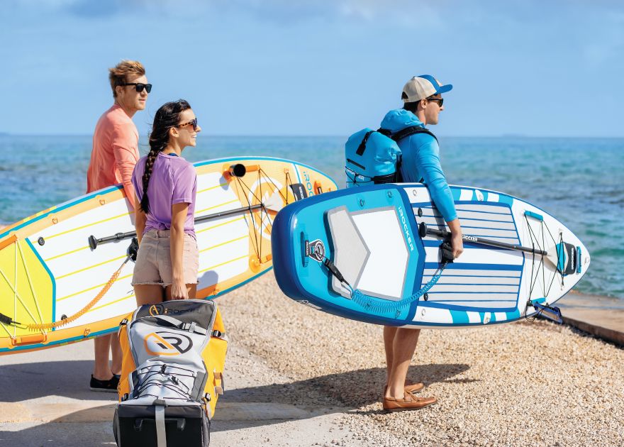 3 people with SUP gear, one holding a paddleboard backpack