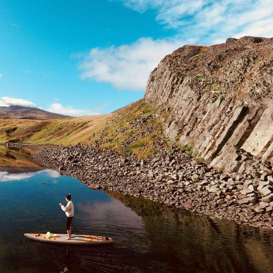 Woman on SUP paddleboard on a lake in front of a rock face