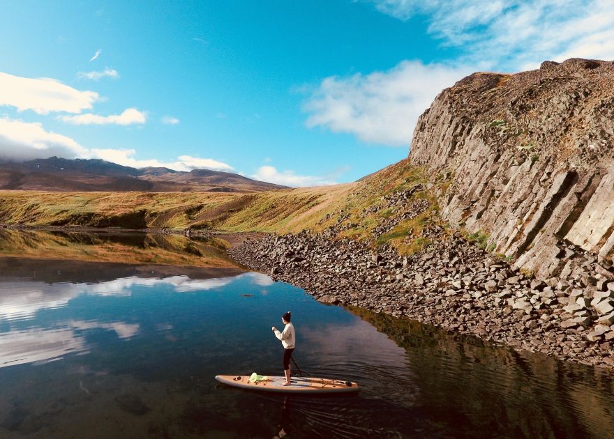 Woman on SUP paddleboard on a lake in front of a rock face