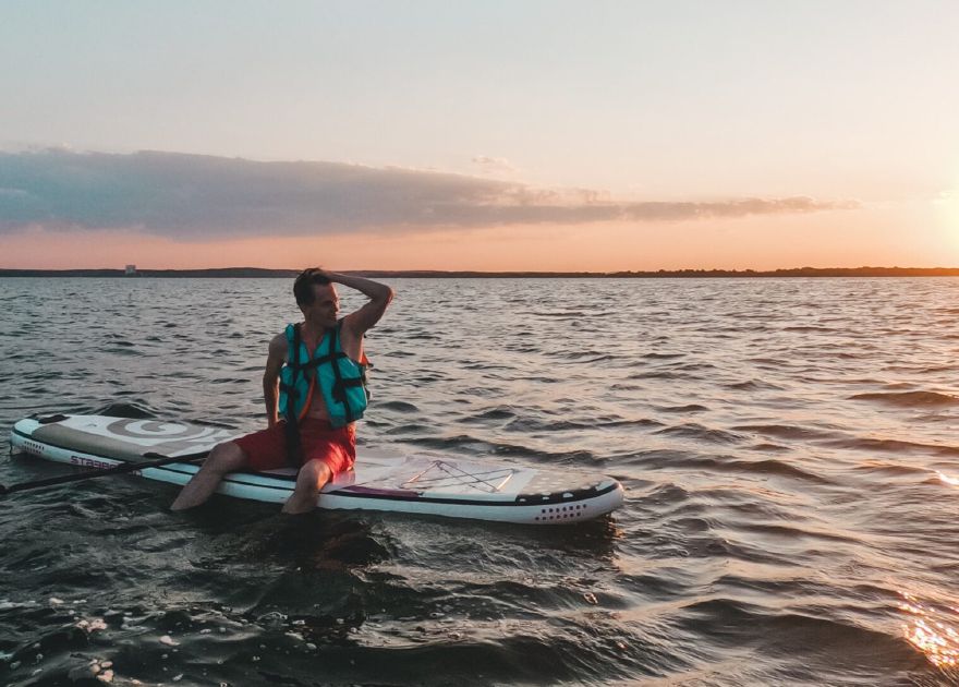 Man sitting on SUP paddleboard with lifevest on and sunset