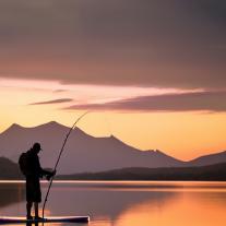 Person stand up paddleboarding while fishing