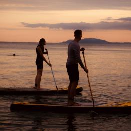 Two people on paddleboards on the water with sunset