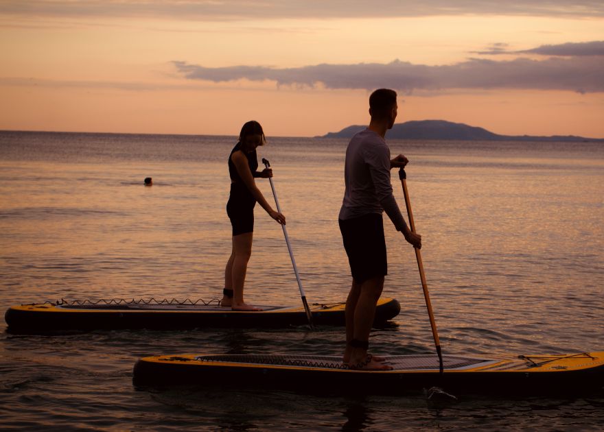 Two people on paddleboards on the water with sunset